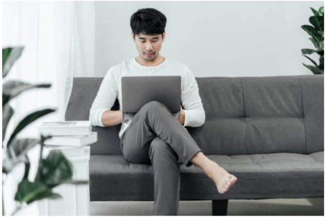 Young man sitting on a sofa with his legs crossed using a laptop